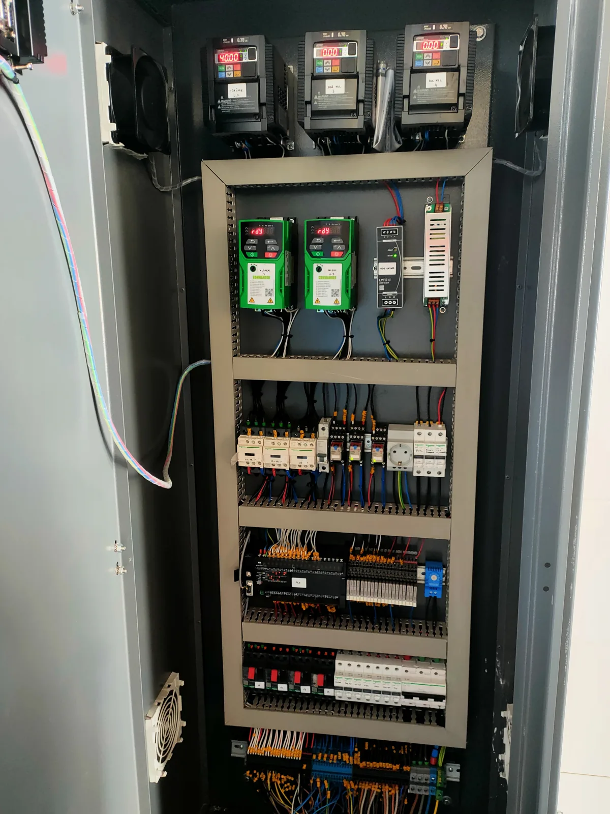 Open electrical control cabinet with three drive units across the top and rows of relays, breakers and terminal blocks below