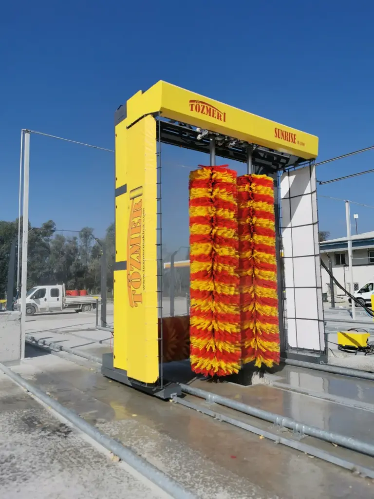 Yellow wash gantry with red and yellow brushes standing empty on its rails outdoors